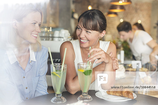 Smiling women drinking lemonade at cafe table