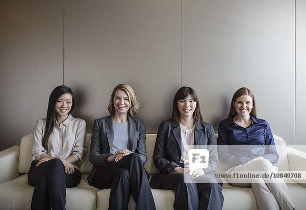 Portrait smiling businesswomen sitting in a row on sofa