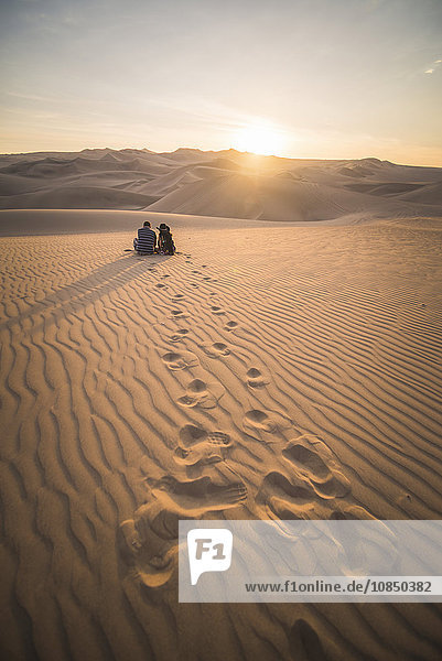 Couple watching the sunset over sand dunes in the desert at Huacachina  Ica Region  Peru  South America