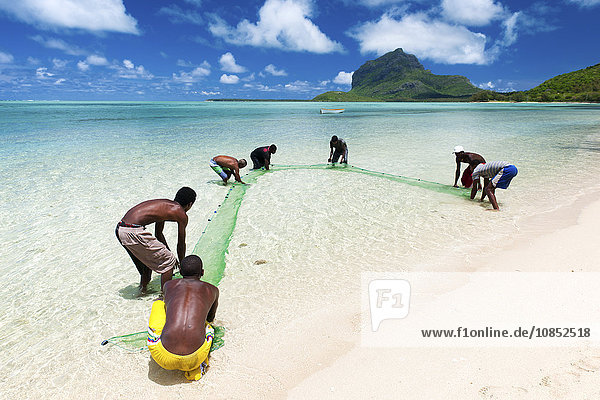 Fisherman on a beach being overlooked by the basaltic monolith  Le Morne  Black River  Mauritius  Indian Ocean  Africa