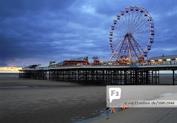 Big wheel and amusements on Central Pier at sunset with young women looking on  Blackpool  Lancashire  England  United Kingdom  Europe