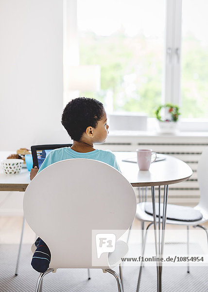Rear view of boy looking away while sitting on chair at home