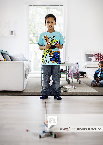 Boy playing with remote controlled airplane at home with brother sitting in background