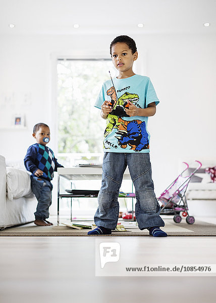Full length of boy holding remote of model airplane at home with brother in background