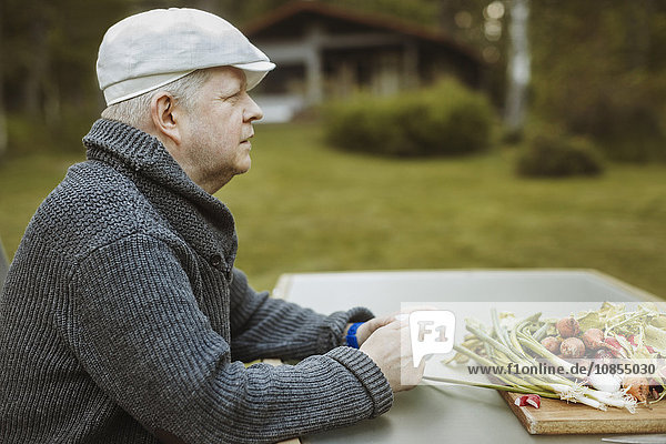 Side view of mature man sitting at table with freshly harvested vegetables