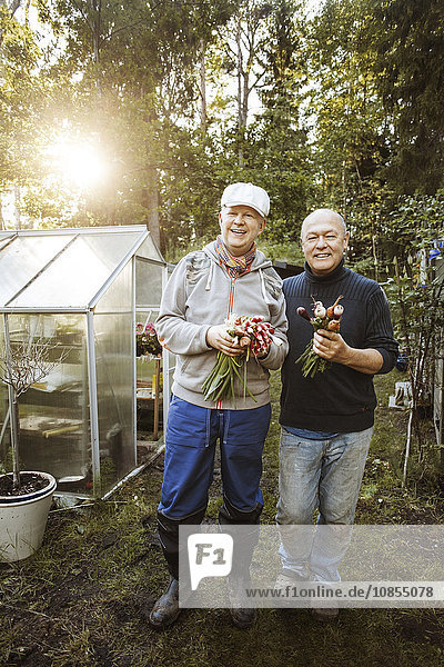 Portrait of happy gay couple holding fresh root vegetables at garden