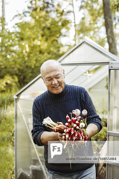 Happy gay man holding fresh root vegetables at garden
