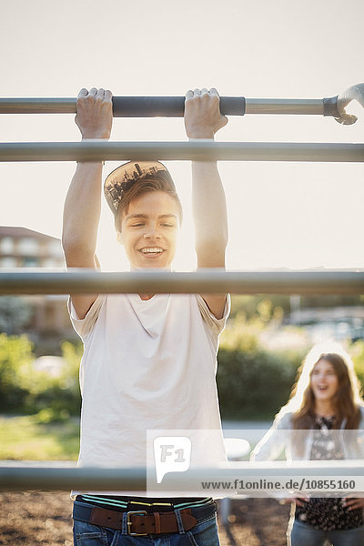 Happy teenager hanging from monkey bars at park