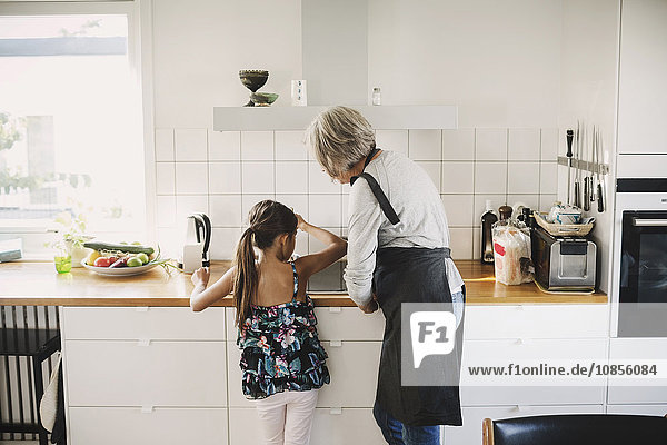 Rear view of girl standing with grandmother preparing food in kitchen