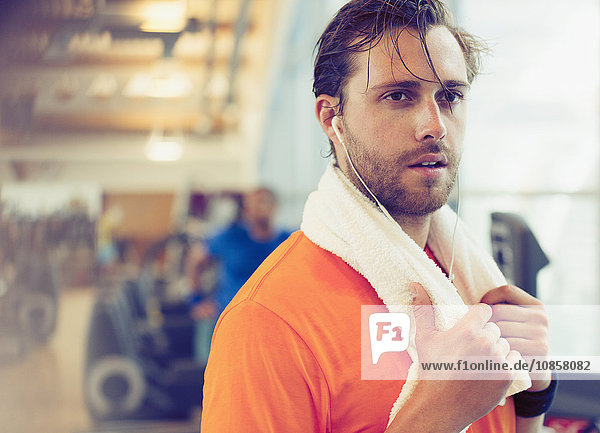 Sweating man with towel and headphones resting in gym
