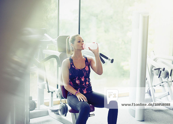 Woman drinking water at exercise equipment in gym