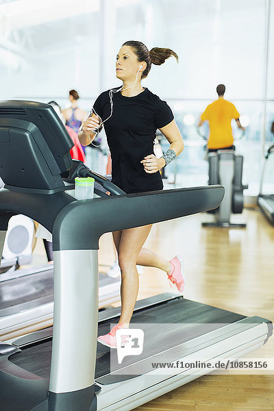 Woman running on treadmill with headphones at gym