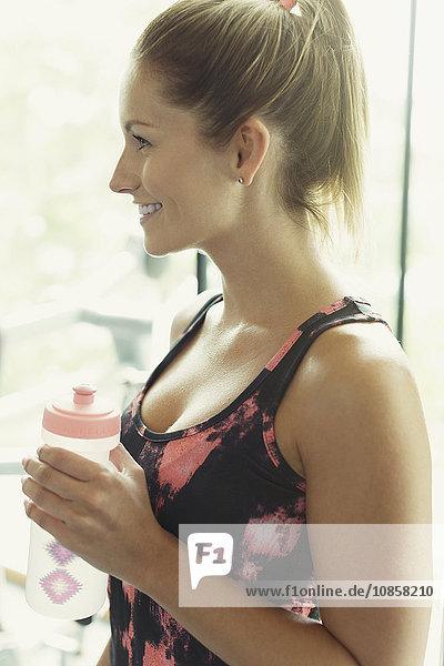Lächelnde Frau trinkt Wasser im Fitnessstudio