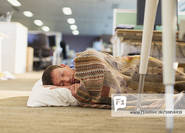 Businessman with pillow and blanket sleeping on office floor
