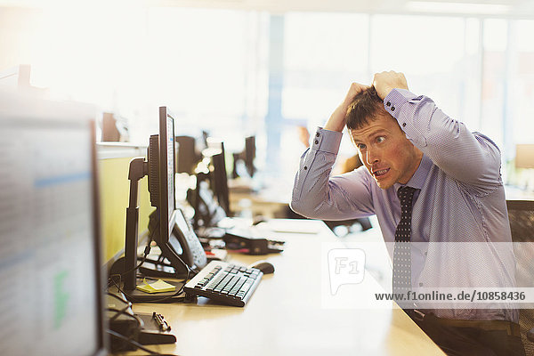 Gestresster Geschäftsmann der sich am Computer im Büro die Haare auszieht.