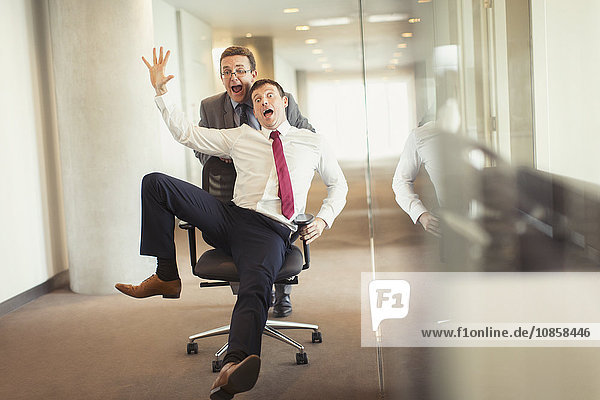 Playful businessman pushing colleague down corridor in office chair
