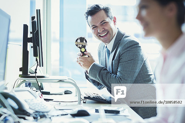 Portrait of enthusiastic businessman holding winner trophy at desk in office