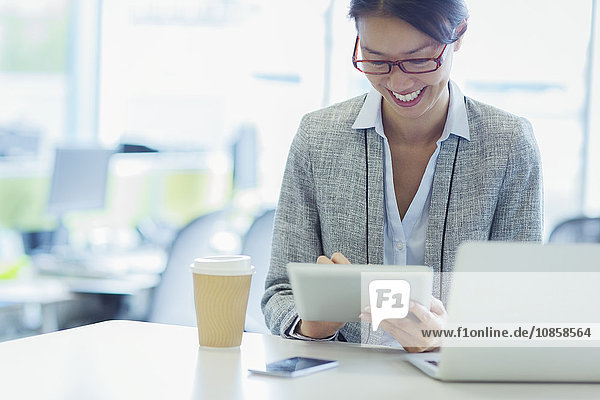 Lächelnde Geschäftsfrau mit digitalem Tablett und Kaffee im Büro
