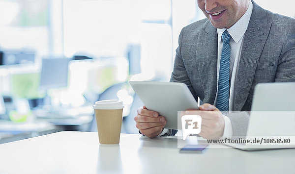 Lächelnder Geschäftsmann mit digitalem Tablett und Kaffee im Büro