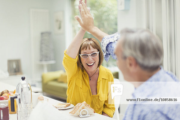 Enthusiastic mature couple high-fiving at breakfast