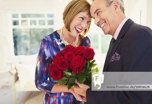 Affectionate well-dressed mature couple with rose bouquet