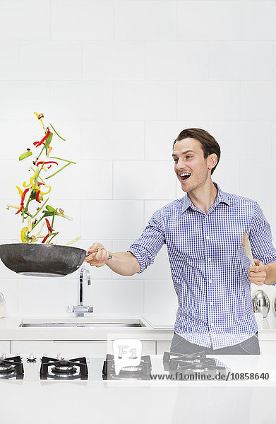 Überraschtes Paar beim Kochen und Wenden von Gemüse in der Pfanne in der Küche