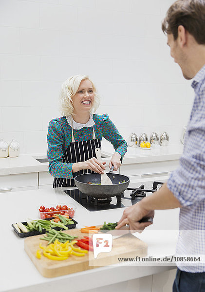 Lächelndes Paar beim Schneiden und Kochen von Gemüse in der Küche