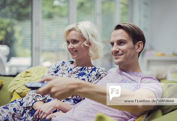 Smiling couple watching TV in living room changing channels