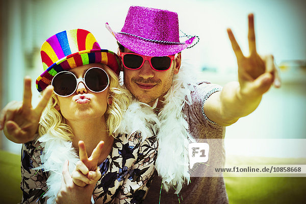 Portrait playful couple in costume sunglasses and hats gesturing peace sign