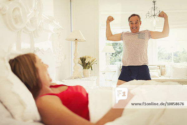 Playful mature man flexing muscles for wife in bedroom