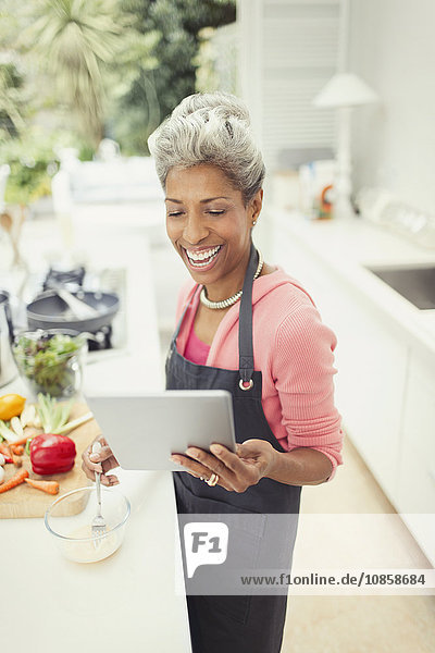 Lächelnde reife Frau mit digitalem Tablettenkochen in der Küche