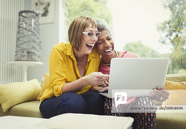 Lachende reife Frauen teilen Laptop auf Wohnzimmer-Sofa
