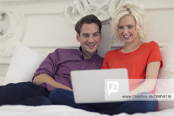 Lächelndes Paar mit Laptop im Bett