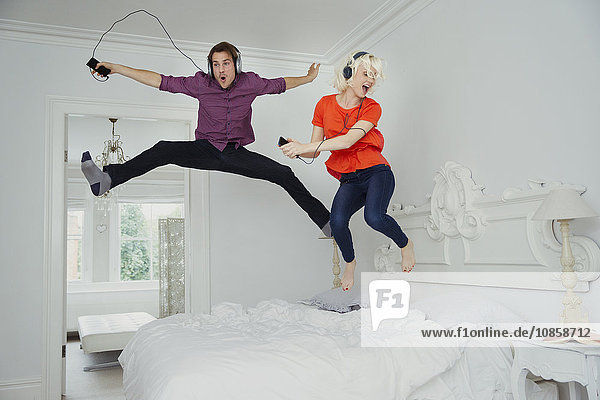 Verspieltes Paar  das auf dem Bett springt und Musik mit mp3-Player und Kopfhörer hört.