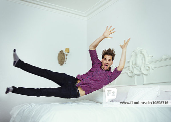 Portrait playful man jumping onto bed