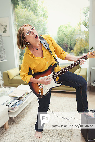 Playful mature woman playing electric guitar in living room