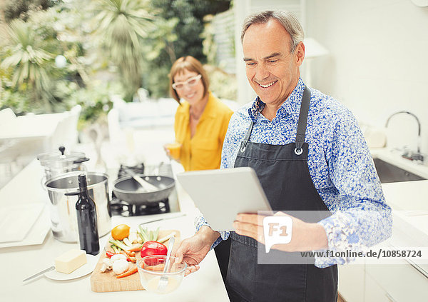 Mature couple with digital tablet cooking in kitchen