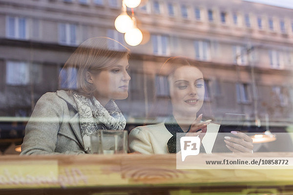 Geschäftsfrauen nutzen Handy am Caféfenster