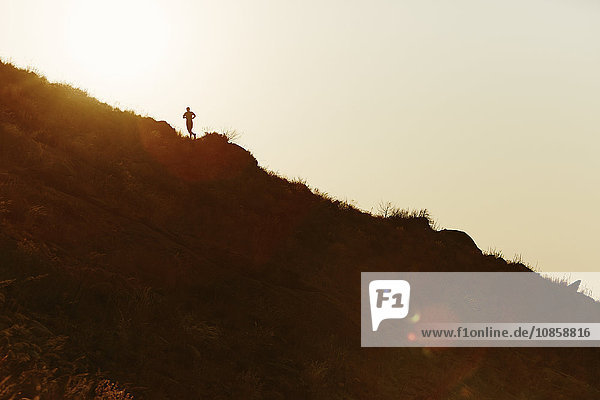 Silhouette of runner ascending hillside at sunset
