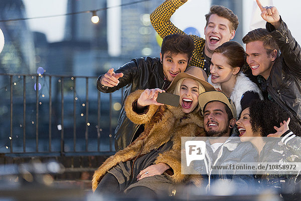 Enthusiastic young adult friends taking selfie at rooftop party