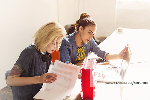 Kreative junge Geschäftsfrauen mit Laptop und Papierkram im Büro