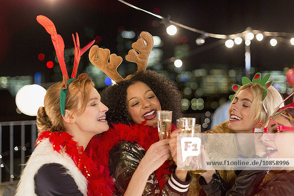 Young women wearing Christmas reindeer antlers and toasting champagne glasses at rooftop party