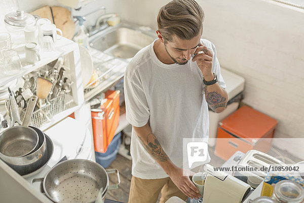 Man using espresso maker and talking on cell phone in apartment kitchen