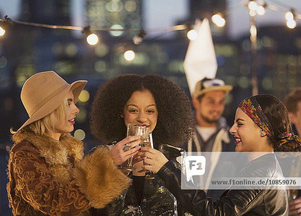 Young women toasting champagne glasses at nighttime rooftop party