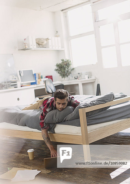 Junger Mann auf dem Bett liegend mit Laptop in der Wohnung