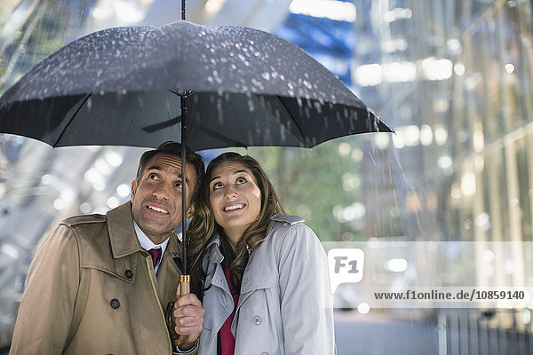 Businessman and businesswoman watching rain under umbrella