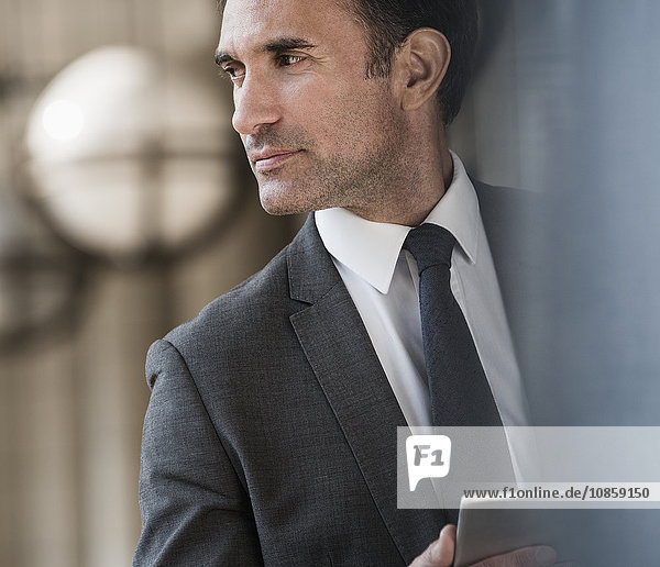 Pensive corporate businessman with digital tablet looking away