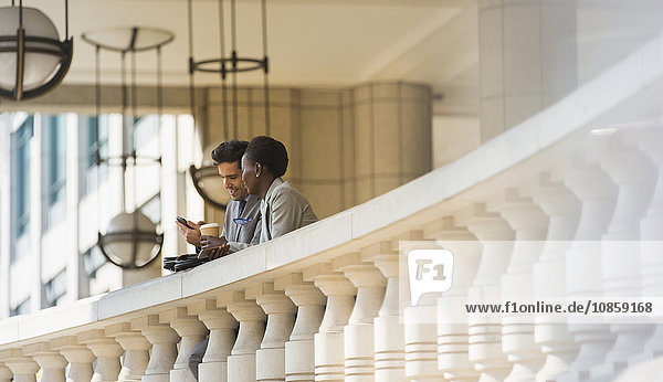 Corporate businessman and businesswoman with coffee and cell phone at railing
