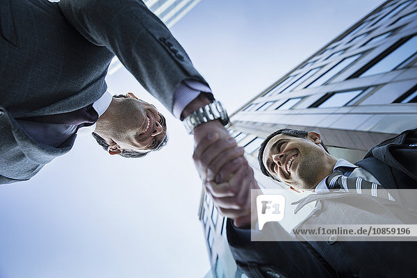 Corporate businessmen handshaking below building