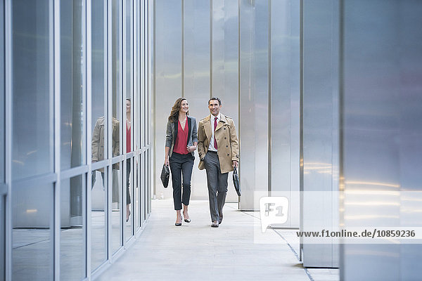 Corporate businessman and businesswoman walking along modern building